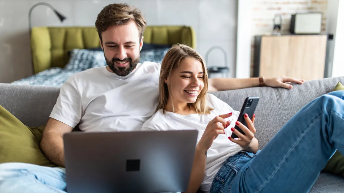 Para relaksująca się na kanapie z laptopem i telefonem